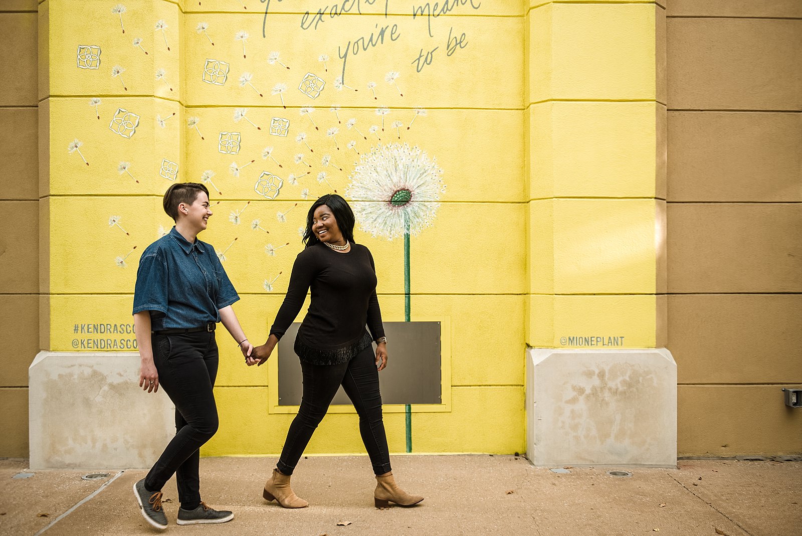 Interracial lesbian couple walking in front of a yellow mural
